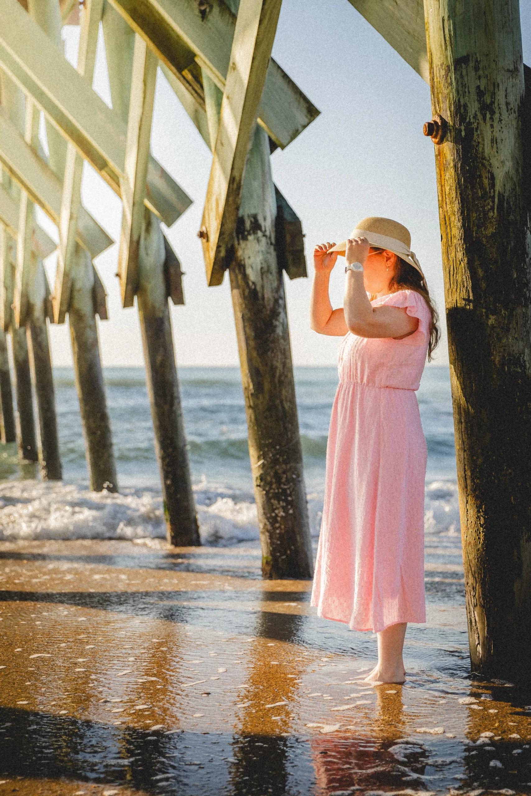 About-me-Adelaide with a woman looking towards the sunrise as she stands under a pier next to the waves on the beach